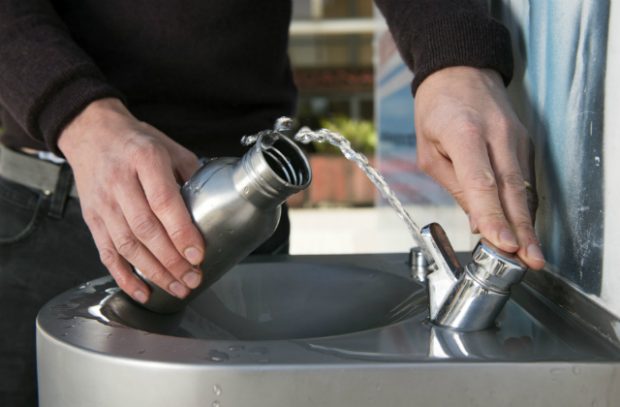 Image shows a person filling up a drinks bottle with water