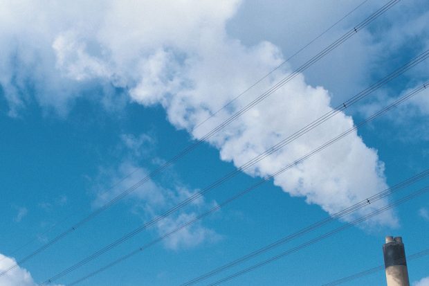 An image of factory with a plume of smoke against a bright blue sky.