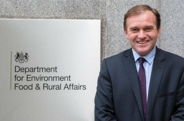 Minister Eustice standing against a sign which says 'Department for Environmnet Food and Rural Affairs'.