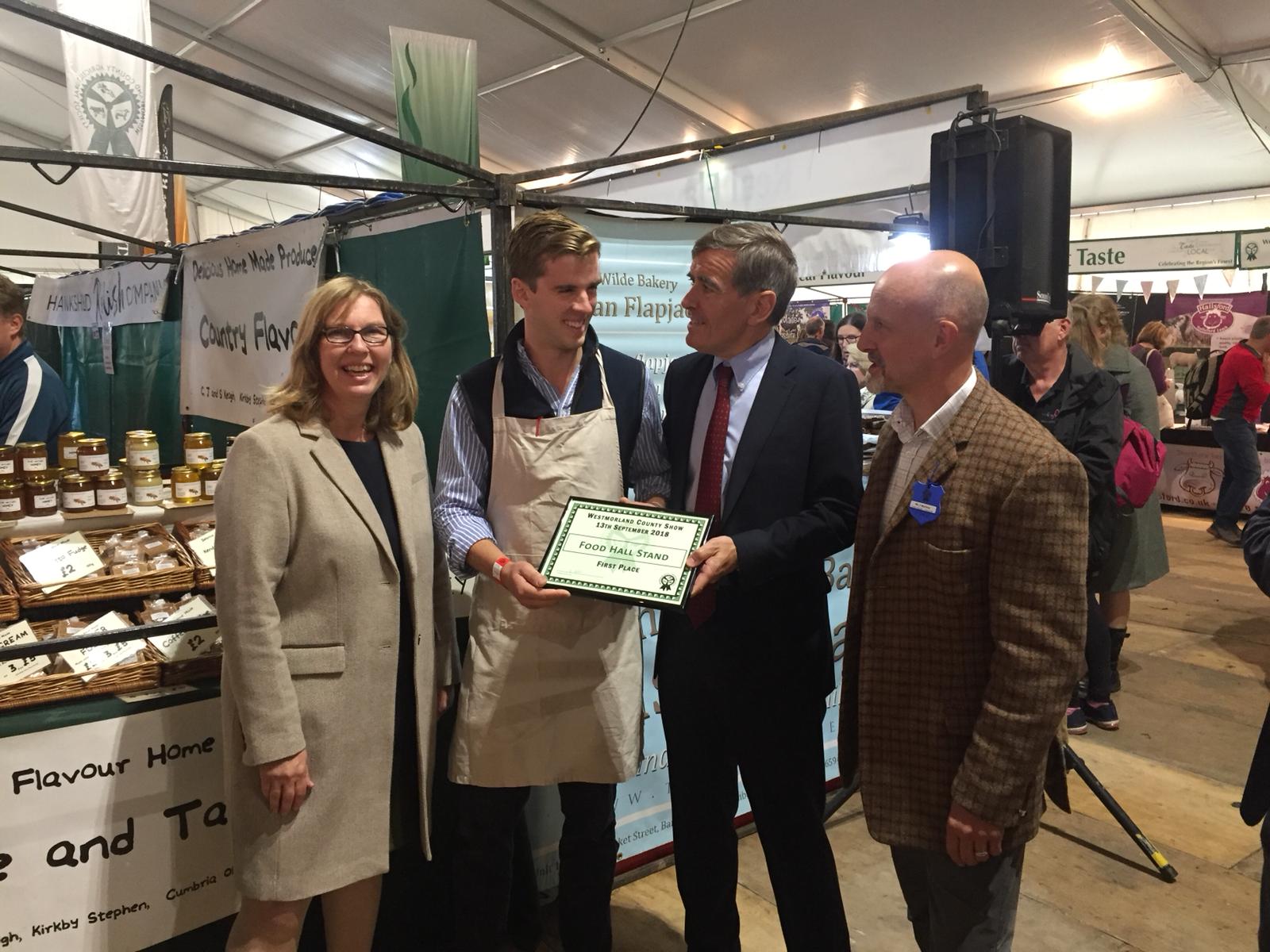 An image of Defra Minister David Rutley meeting farmers and food producers at Westmorland Show. He is holding a 'first place' sign.