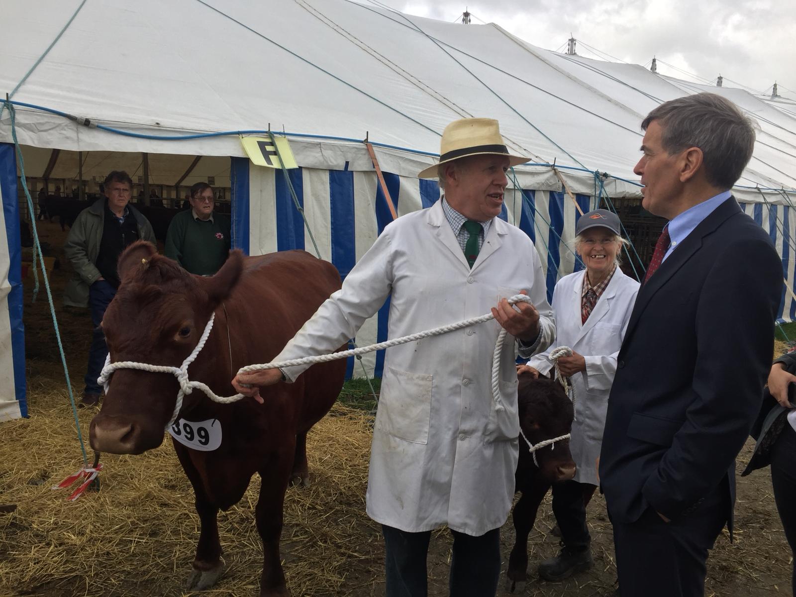 An image of Defra Minister David Rutley talking to farmers. The farmer is standing next to a cow.