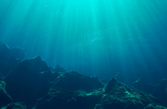 An image of the ocean floor with rocks on the bottom and light shining through the water.