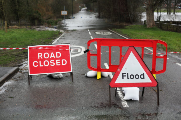 Image of a road closed sign and a flood sign against the backdrop of a road.