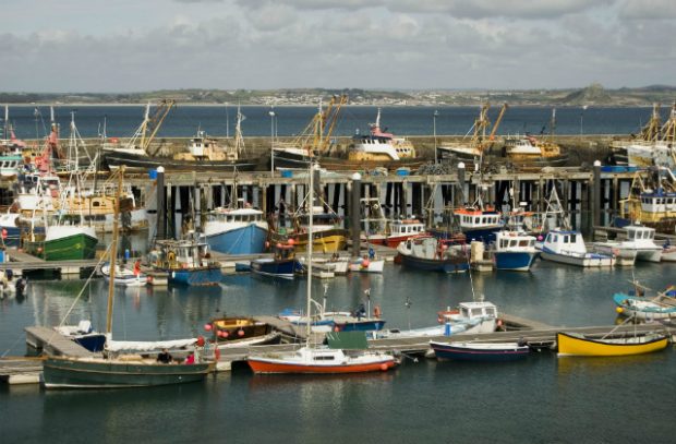 An image of fishing boats in a harbour against a grey sky.