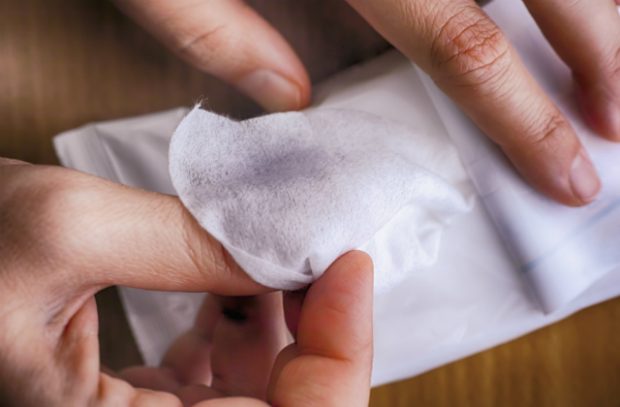 An image of someone's hands holding a wet wipe with dark makeup on it.