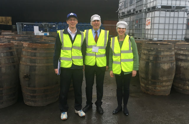 An image of Minister Rutley standing at a liquor factory wearing a high vis vest surrounded by two other people.