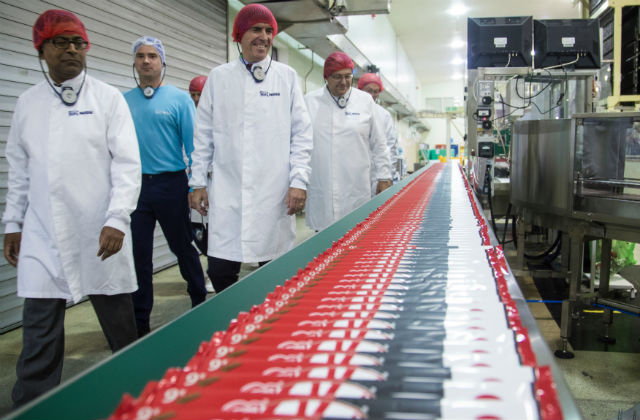 An image of Minister Rutley and several other people walking past a supply chain conveyor belt at the Nestle factory.