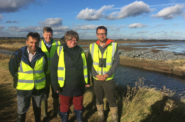 An image of Minister Coffey standing in a flood management area wearing a high vis vest surrounded by three other people.