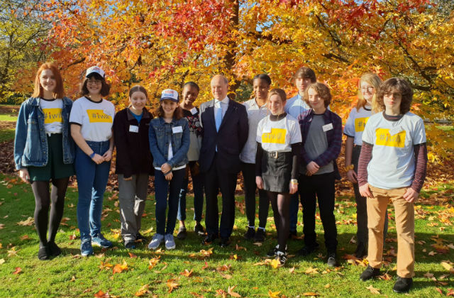 An image of Lord Gardiner standing against a wooded backdrop surrounded by young environment ambassadors.