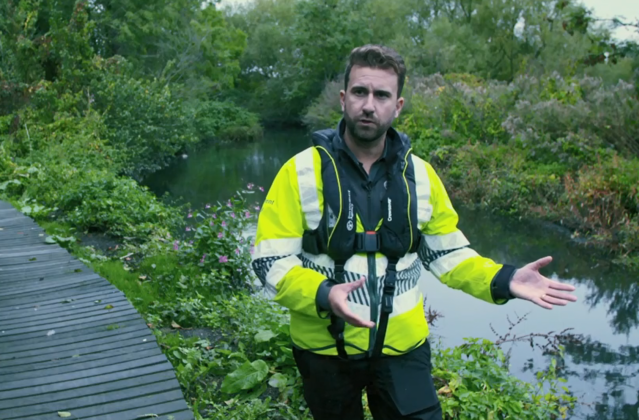 An image of Environment Agency officer Mathew Reed explaining his work investigating Symphony Chauffeurs, standing next to a body of water wearing a high vis jacket.