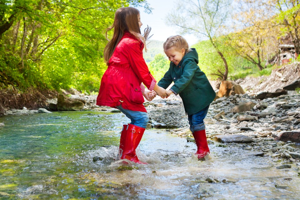 Image of two children in raincoats jumping in a puddle.