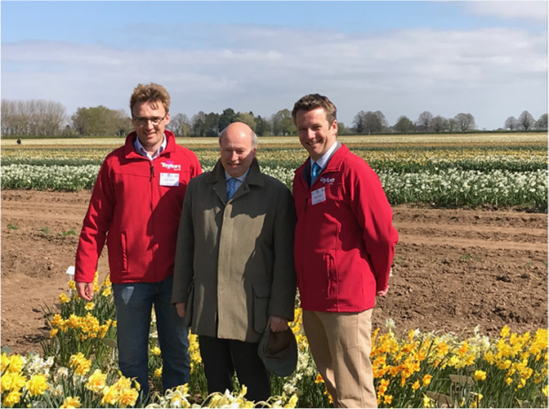 Lord Gardiner and two men in red jackets standing in front of daffodil field