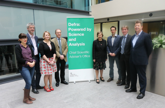 The Systems Research Programme fellows and CSA Ian Boyd standing in a row in front of a banner which reads ‘Defra: Powered by Science and Analysis, Chief Scientific Adviser’s Office’. 