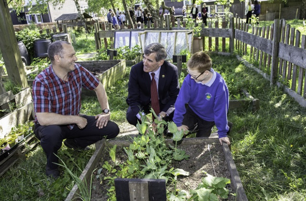 Image of Minister David Rutley, a teacher and a pupil sat next to a raised bed of plants