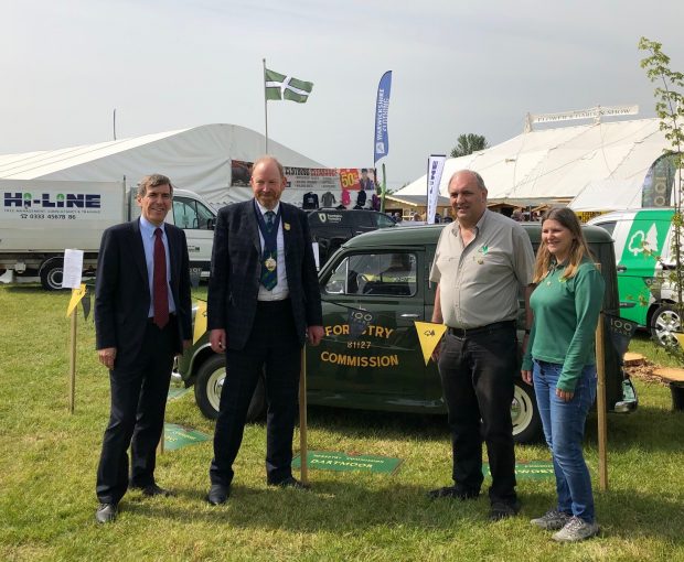 image of minister Rutley, sir Harry Studholme and two members of the forestry commission standing in a field in front of a green car. The car has a sign on the door saying ‘forestry commission’.