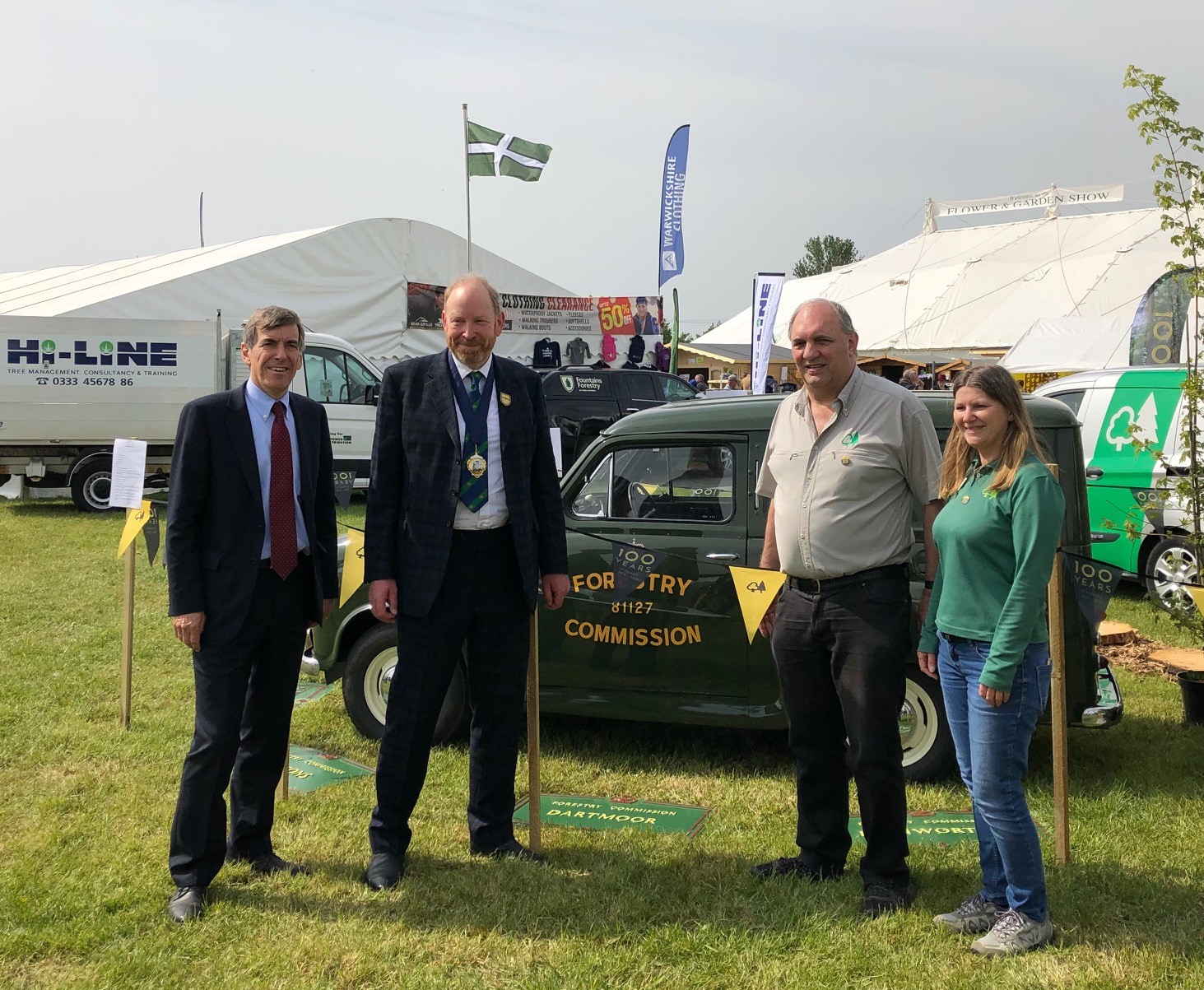 image of minister Rutley, sir Harry Studholme and two members of the forestry commission standing in a field in front of a green car. The car has a sign on the door saying ‘forestry commission’.