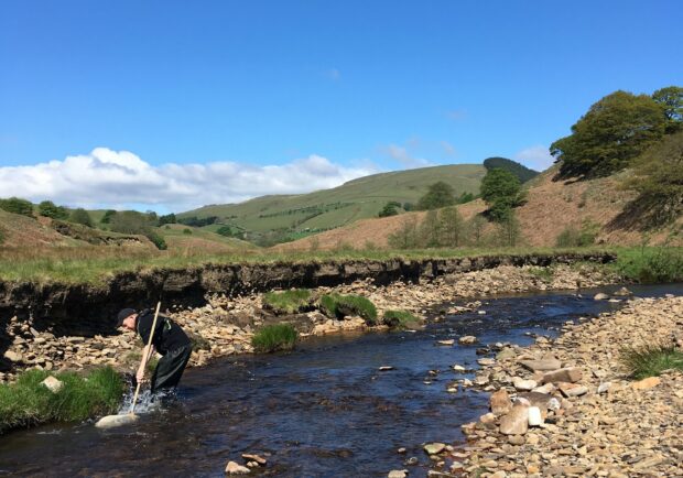 A photo of an Environment Agency employee taking sample of a river for quality testing. 