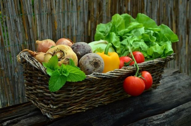 A brown wicker basket of vegetables including lettuce, tomatoes and peppers on a brown background. 