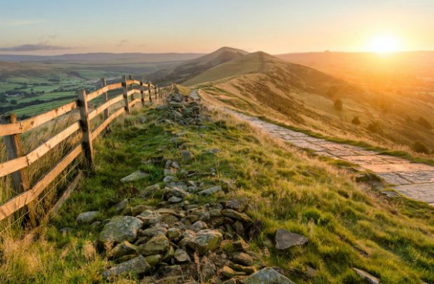 A sunset over a range of hills, with a footpath and fence running through it