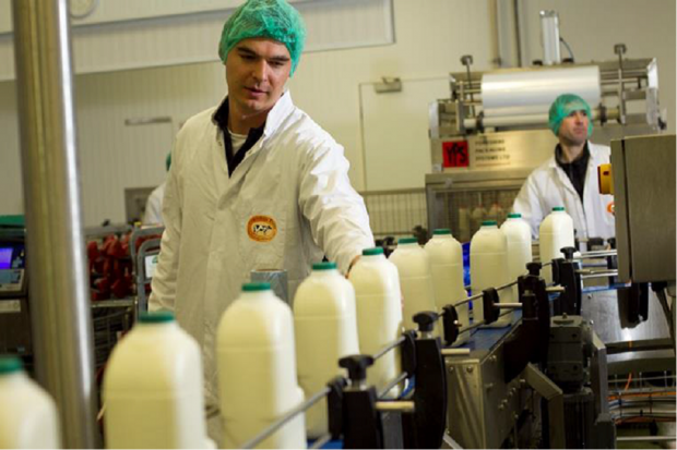 Two men at a milk processing unit where bottles of milk sit on a production line