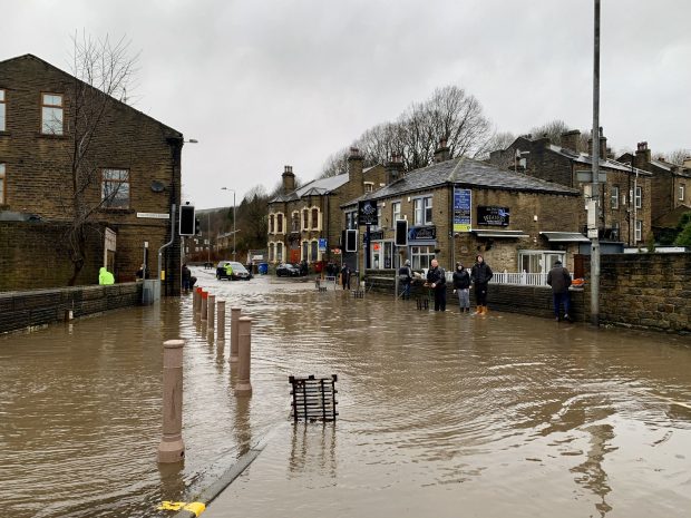 A flooded road lined with houses with several people standing in water 