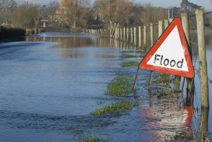 A flood warning sign, on a closed country road next to water logged fields in the Avon Valley, Hampshire, England. Flooded after an extreme amount of rainfall at the start of 2014