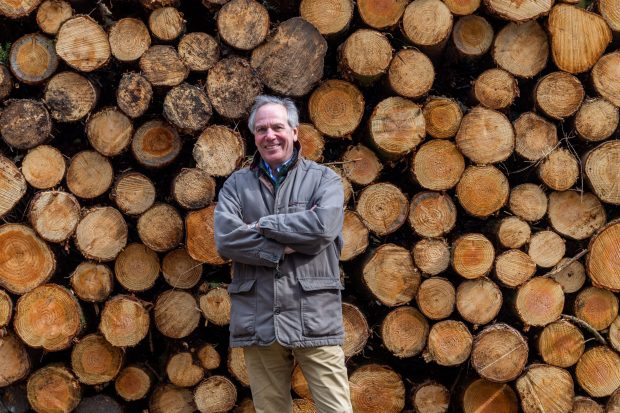 Image of Sir William Worsley standing in front of log pile