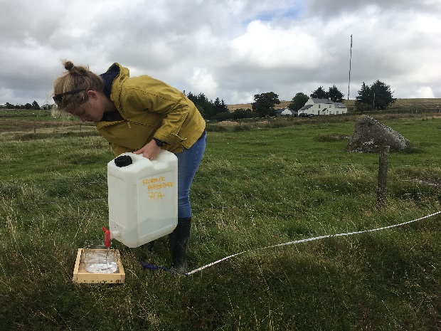 A scientist stands in a field with a plastic canister ready to conduct an experiment