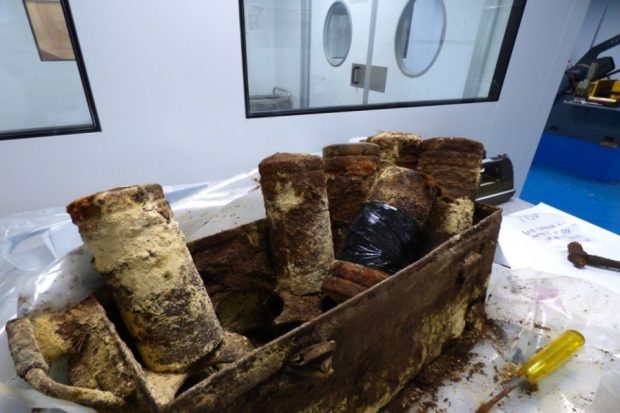 A rusted and dirty box containing numerous mustard gas canisters.