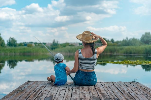 A woman and young boy sat fishing on a dock, facing away from the camera.