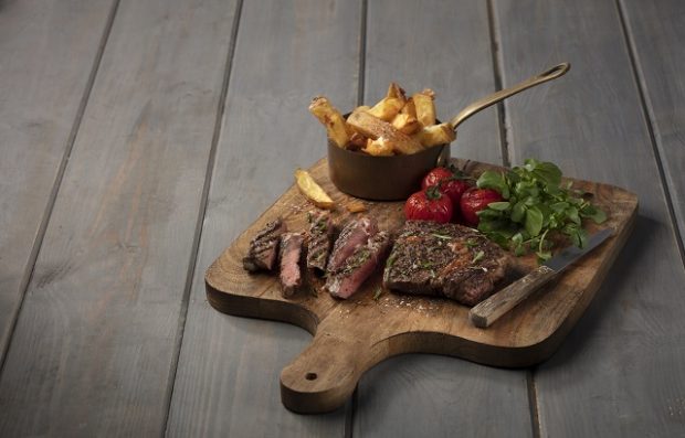 An image of a ribeye steak with vegetables on a wooden board