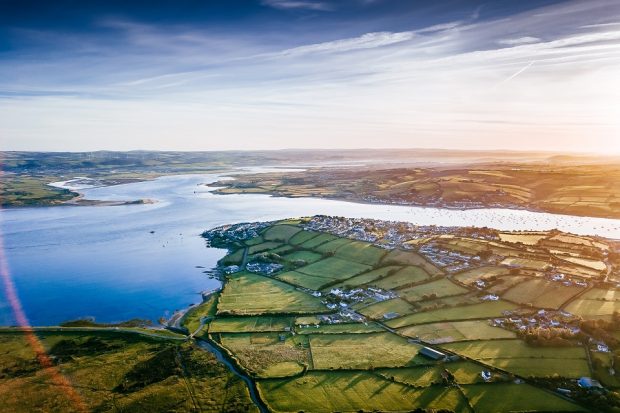 Aerial image of green fields bordering the sea, against a blue sky background.